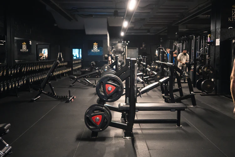 A modern gym featuring weightlifting equipment, dumbbells, and a workout area, with mirrors and a sleek, dark design.