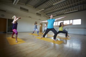 Mixed-gender group taking part in a yoga class on matching yellow matts