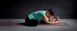 A teacher in a Yin & Restorative yoga CPD course in a pose on the floor using a mat and block