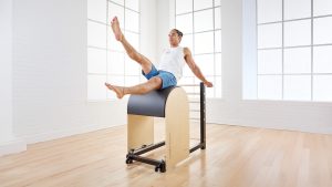 A person is performing an exercise on a pilates ladder barrel in a bright, airy studio with large windows.