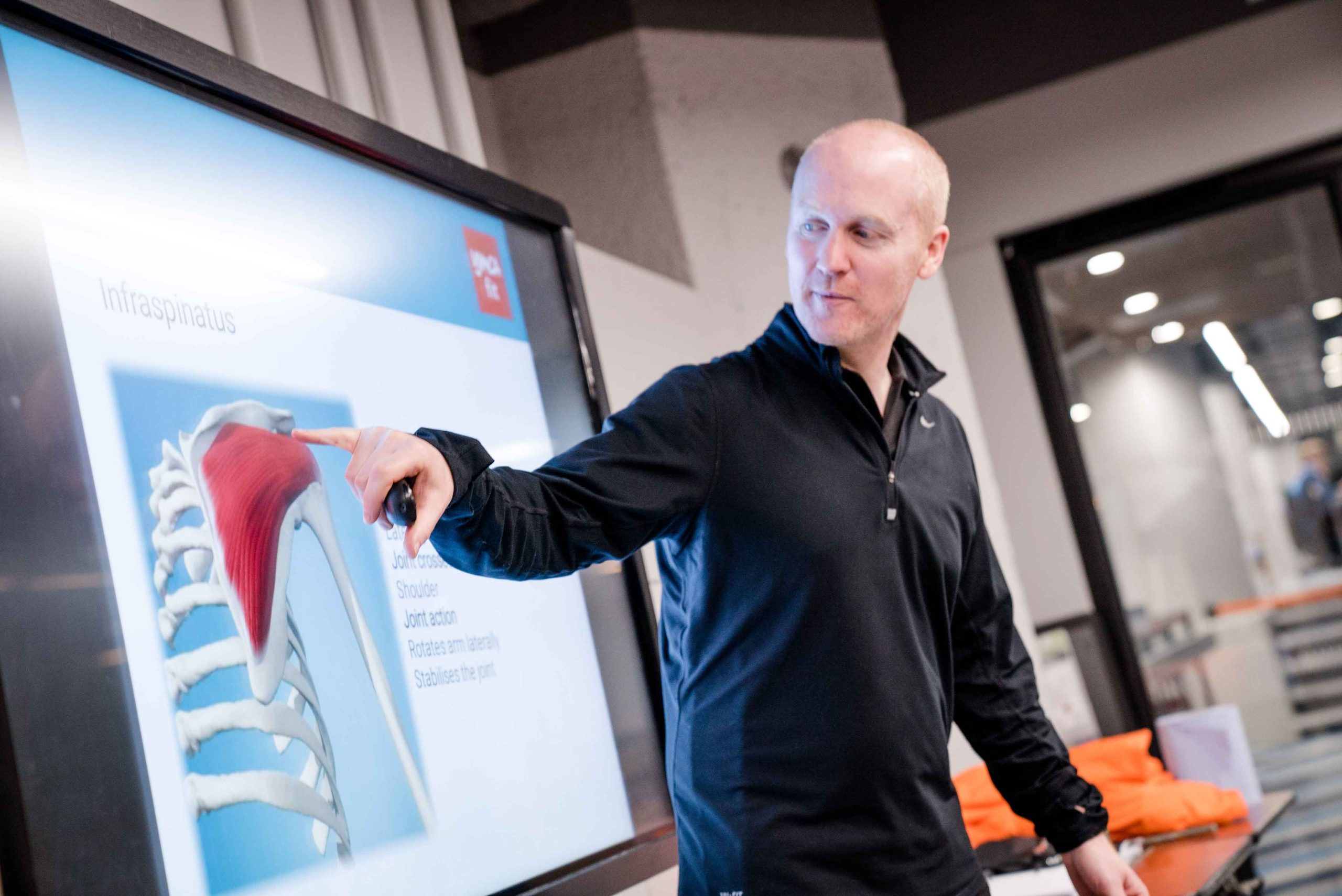 A person points at a presentation about the infraspinatus muscle and its role in shoulder movement, with anatomical visuals displayed.