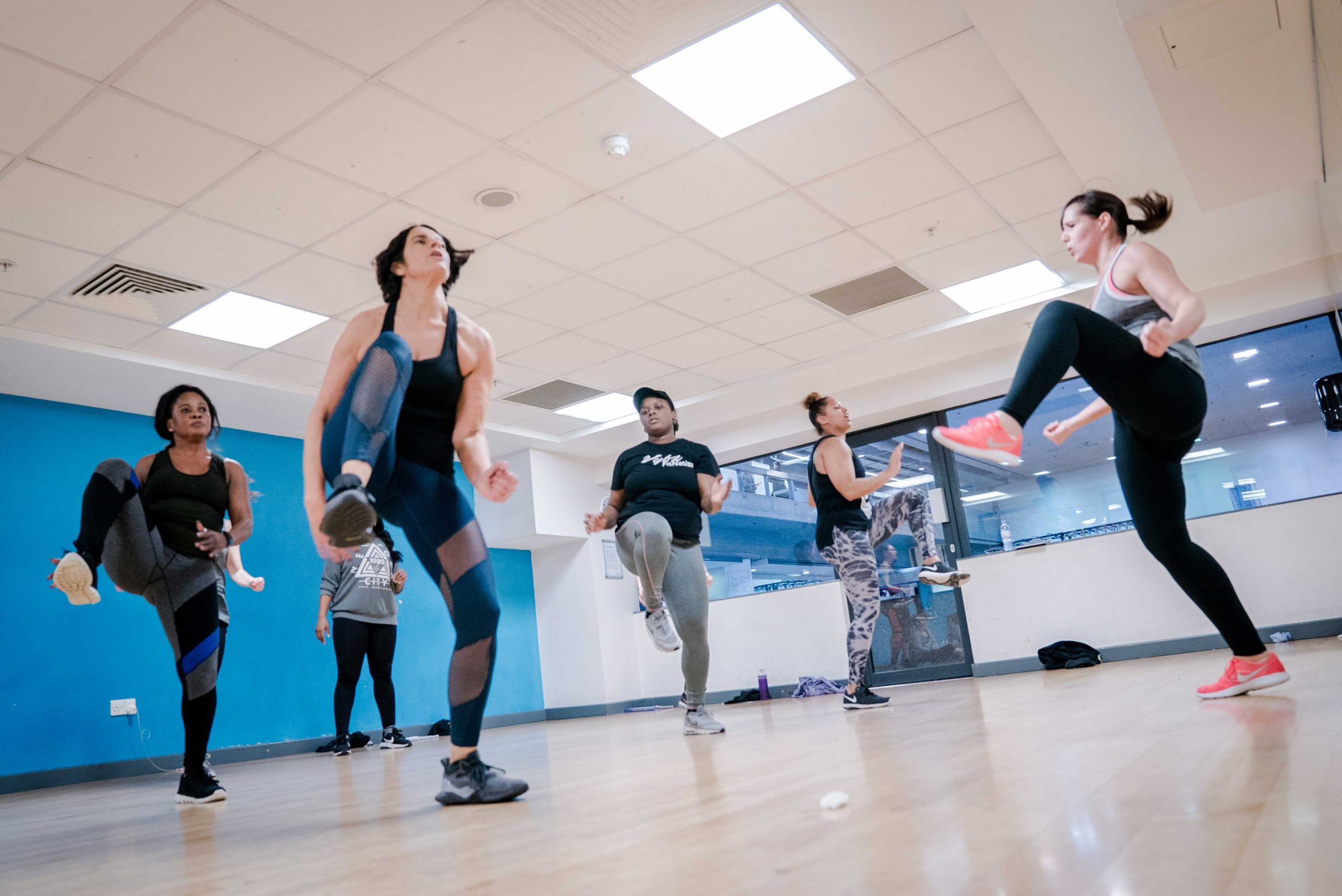 Group of diverse women exercising in a bright fitness studio, performing high knee kicks during a workout session.