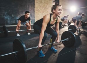Group of people lifting barbells during a workout session in a gym with bright lighting and rubber flooring.