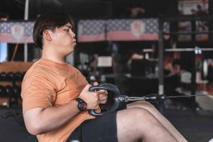 Person in orange shirt using a seated cable row machine in a gym .