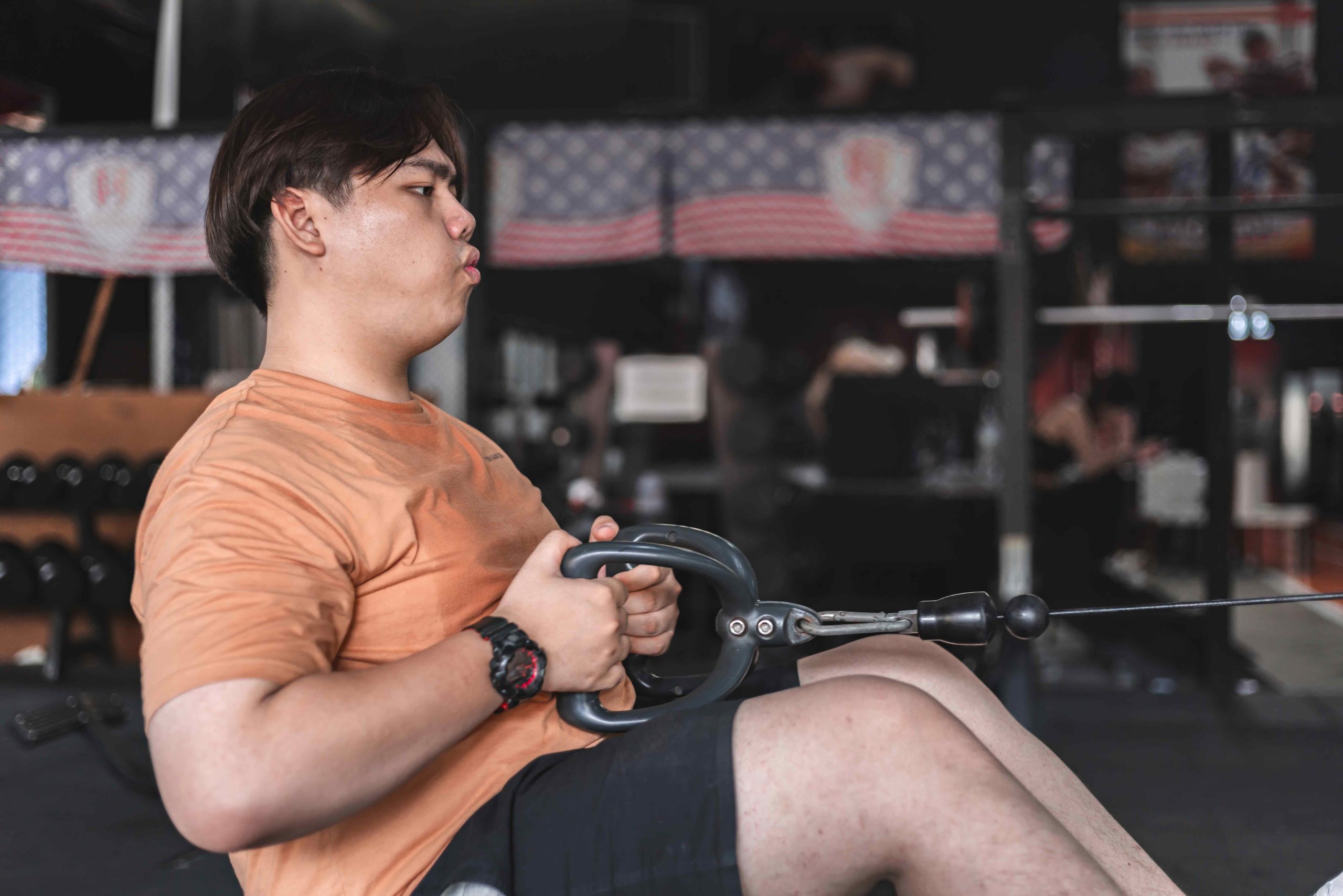 Person in orange shirt using a seated cable row machine in a gym .