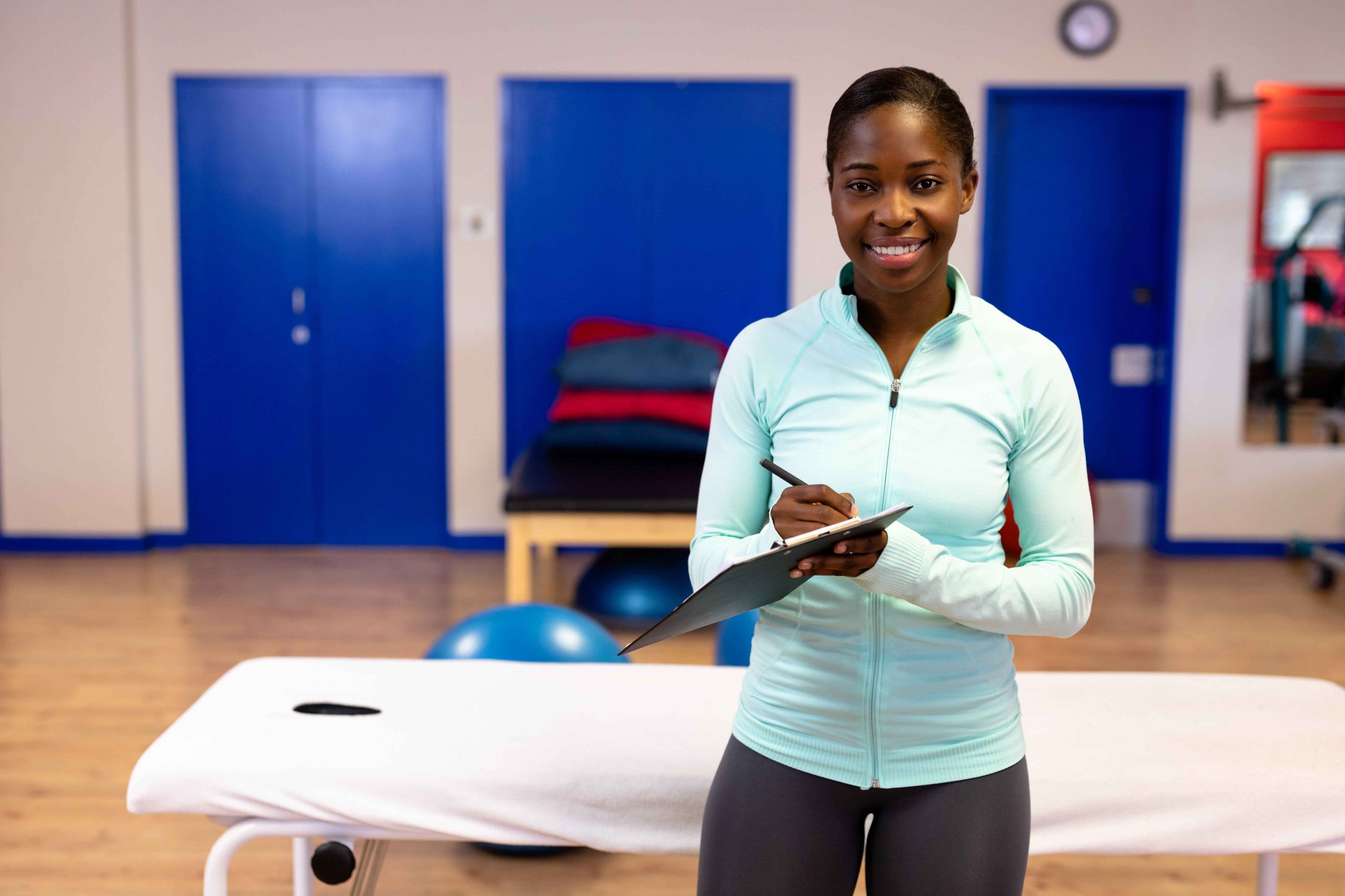 Smiling woman in gym attire, clipboard.