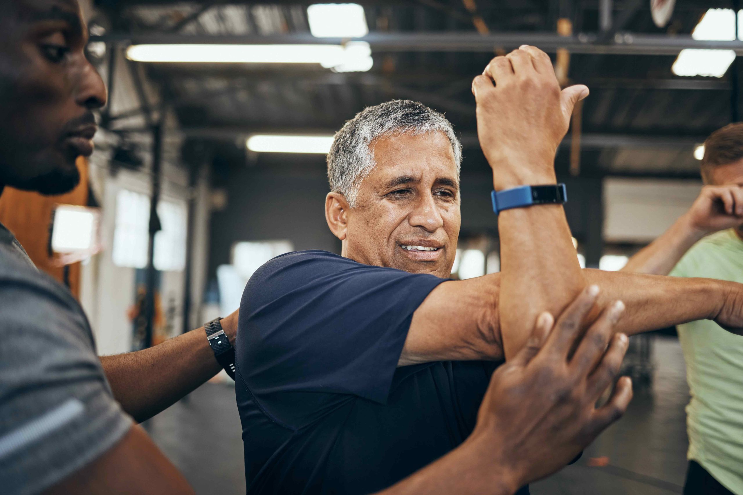 Trainer assisting an older man with arm stretches in a gym setting, focusing on mobility and flexibility exercises.
