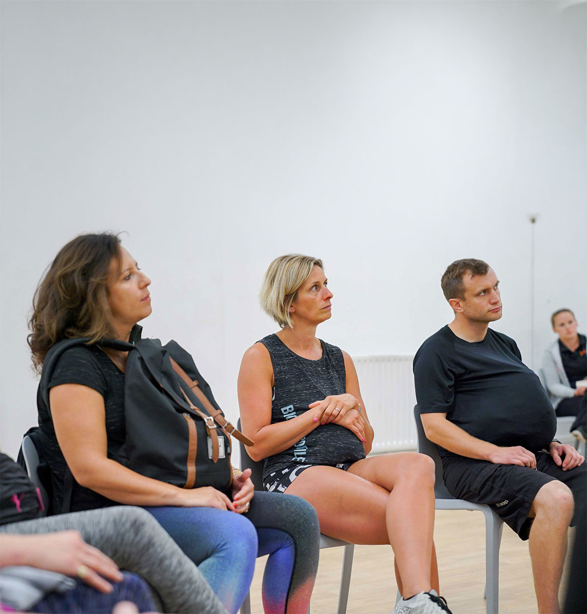 Group of people sitting indoors, with two wearing pregnancy simulation suits, participating in a prenatal experience session.